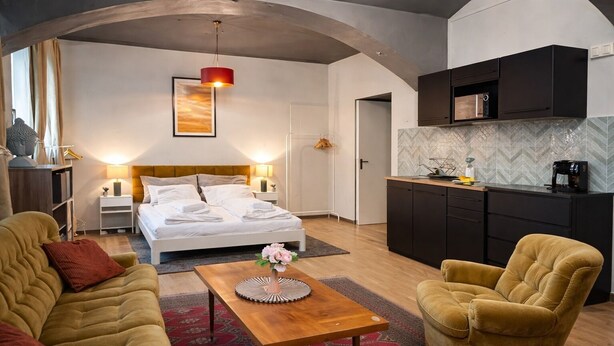 Ett modernt hotellrum med en säng, en soffa, en stol, ett litet bord, ett köksutrymme och en unik takdesign.