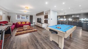 A modern living room with a pool table, red sofas, and a kitchen area with dark cabinets and a built-in oven. - Rainfall Shower | Pool/Snooker | x 4 Cars (Berkshire)