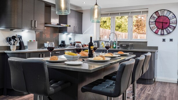 A modern kitchen with a central island, bar stools, and a large wall clock. - Rainfall Shower | Pool/Snooker | x 4 Cars (Berkshire)