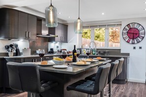 A modern kitchen with a central island, bar stools, and a large wall clock. - Rainfall Shower | Pool/Snooker | x 4 Cars (Berkshire)