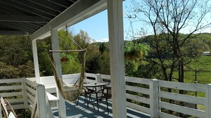 A covered outdoor deck with a hammock, wicker furniture, and a view of a green landscape.