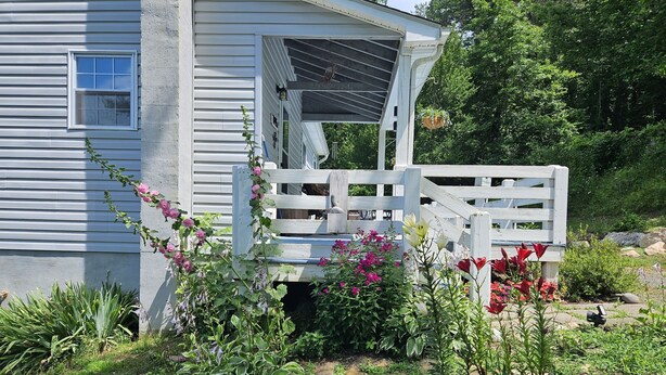 A house with a white exterior, a wooden porch, and a garden with various plants and flowers.