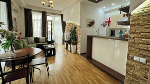 Una sala moderna con un sofá, una mesa de comedor y sillas. Hay una zona de cocina con un refrigerador y una pared de acento de piedra.