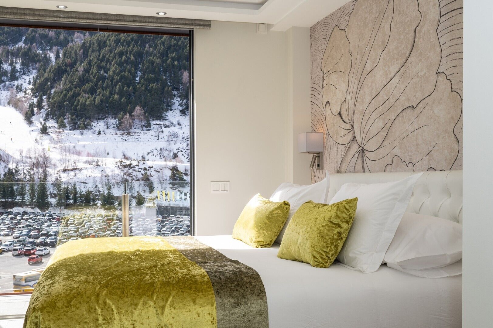 A bedroom with a large window, a bed with white and green pillows, and a wall art piece.