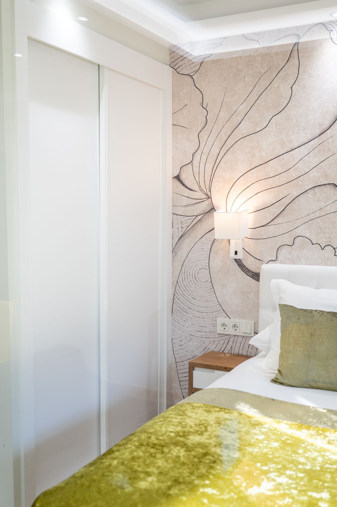 A bedroom with a bed, a nightstand, a wall-mounted lamp, and a closet.