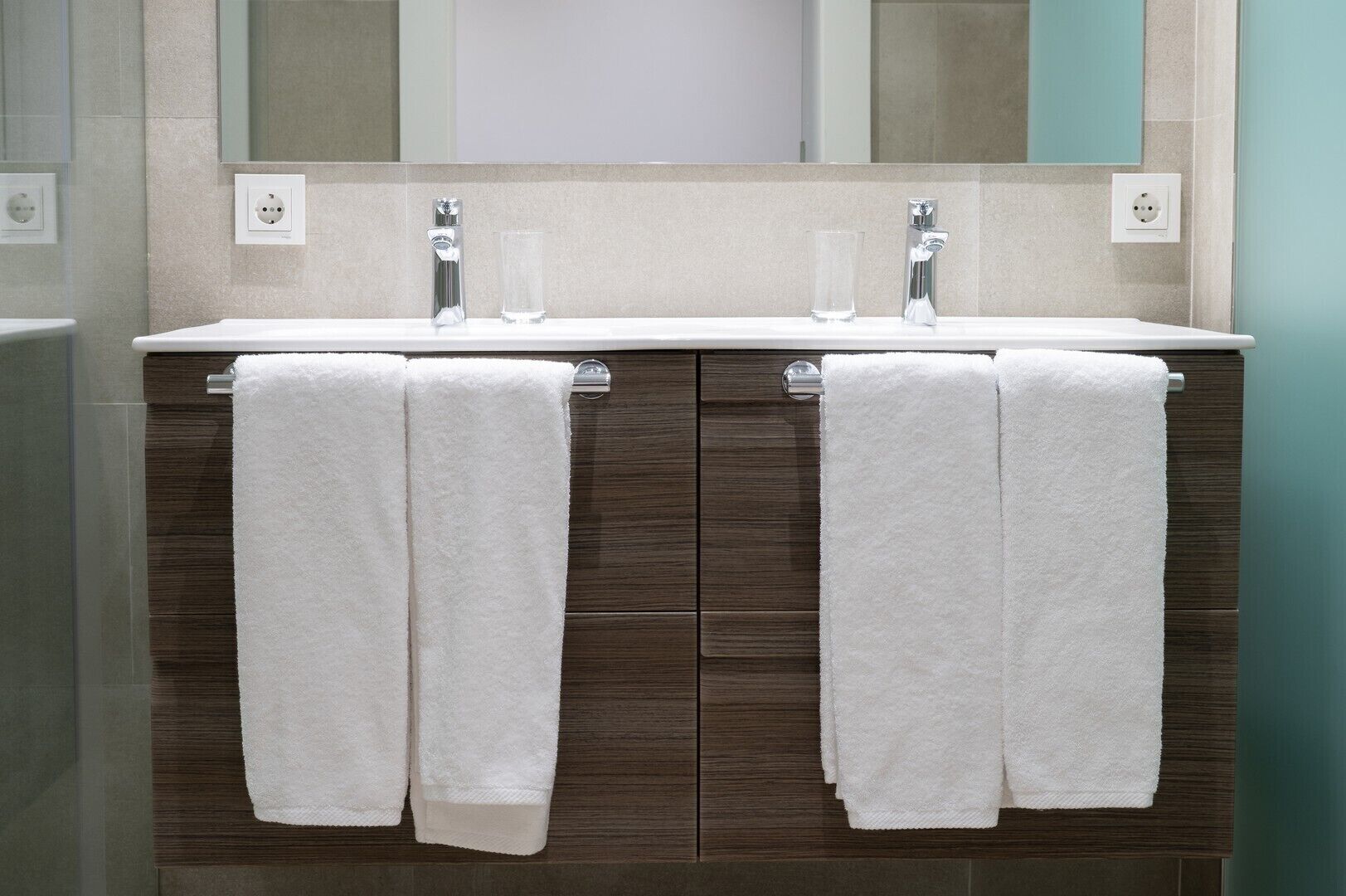 A bathroom with a double sink vanity, two towels hanging on towel racks, and a mirror above the sinks.