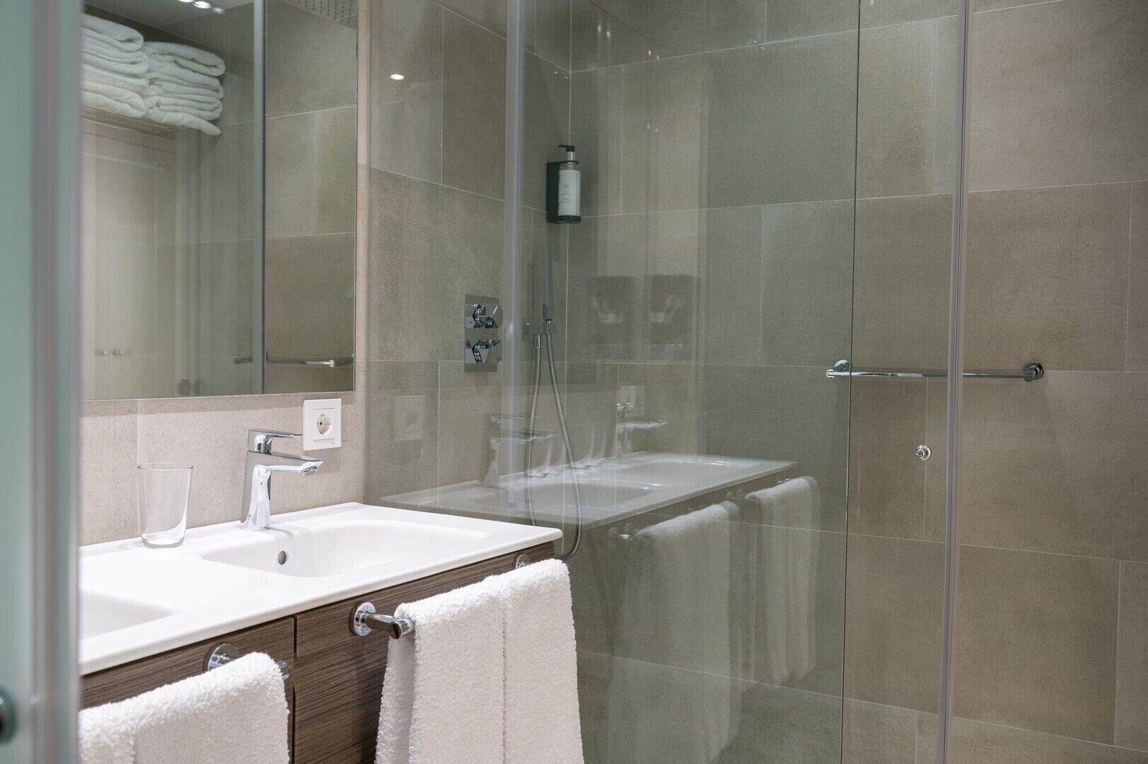 A modern bathroom with a glass shower enclosure, a white sink, and a mirror.
