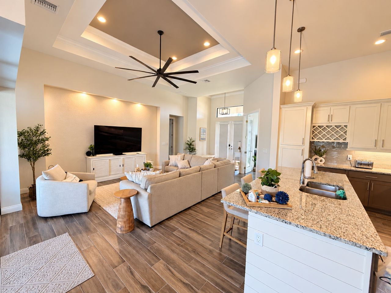 A modern living room with a sofa set, a television, and a kitchen area with a countertop and sink.