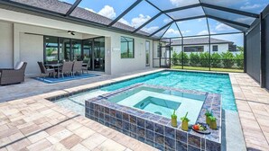 Une piscine extérieure couverte, dotée d’un jacuzzi, et entourée d’une terrasse avec des chaises et une table.