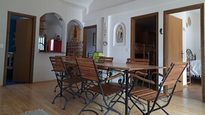 A dining area with a wooden table and chairs, a kitchen in the background, and a doorway leading to another room.
