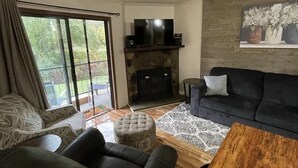 Een woonkamer met een open haard, een televisie en een groot raam met gordijnen.
