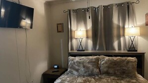 Een slaapkamer met een bed, een plafondventilator, een aan de muur bevestigde televisie en twee bedlampen.