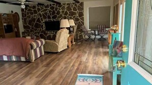 Una sala de estar con pared de piedra, piso de madera, un sofá, una mesa de centro, un televisor y una puerta con marco azul.