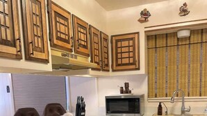 Una cocina con armarios de madera, microondas, lavamanos y ventana con persianas.