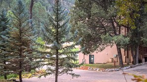 A building surrounded by trees, a paved area, and a staircase leading to an upper level. - Cottages at Canyon Creek #1 (Ruidoso)