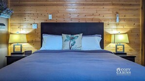 A wooden-paneled room with a bed, two bedside lamps, and a floral pillow. - Cottages at Canyon Creek #1 (Ruidoso)