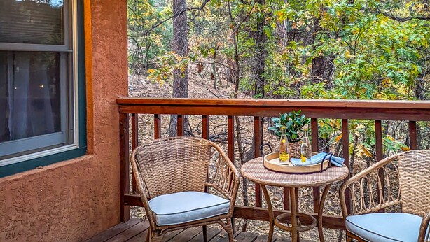 A wooden deck with wicker chairs and a small round table, overlooking a forested area.
