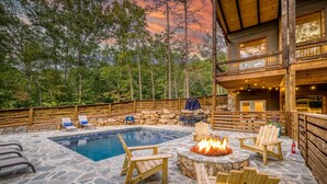 A stone patio with a pool, wooden chairs, and a fire pit. - EPIC Heated pool, Outdoor Fireplace, Pool & Hot Tub! Arcade, and Barrel Sauna (Mineral Bluff)