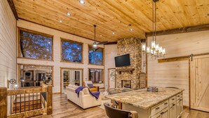 A spacious living area with a large wooden ceiling, a stone fireplace, and a kitchen island with bar stools. - EPIC Heated pool, Outdoor Fireplace, Pool & Hot Tub! Arcade, and Barrel Sauna (Mineral Bluff)