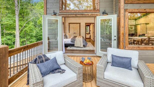 A wooden deck with wicker furniture and a dining table, overlooking a forested area. - EPIC Heated pool, Outdoor Fireplace, Pool & Hot Tub! Arcade, and Barrel Sauna (Mineral Bluff)