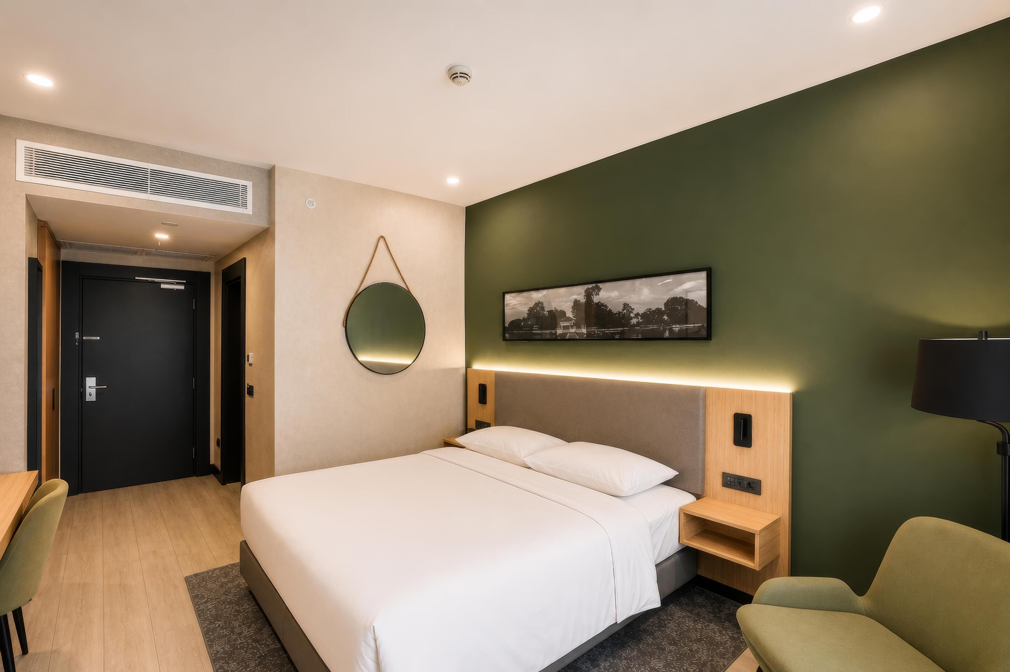 Habitación de hotel con cama, mesita de noche, silla e imagen colgada en la pared.