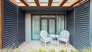 Un espace de détente extérieur moderne, composé de deux chaises et d’une table, et agrémenté d’une pergola en bois et de volets métalliques.