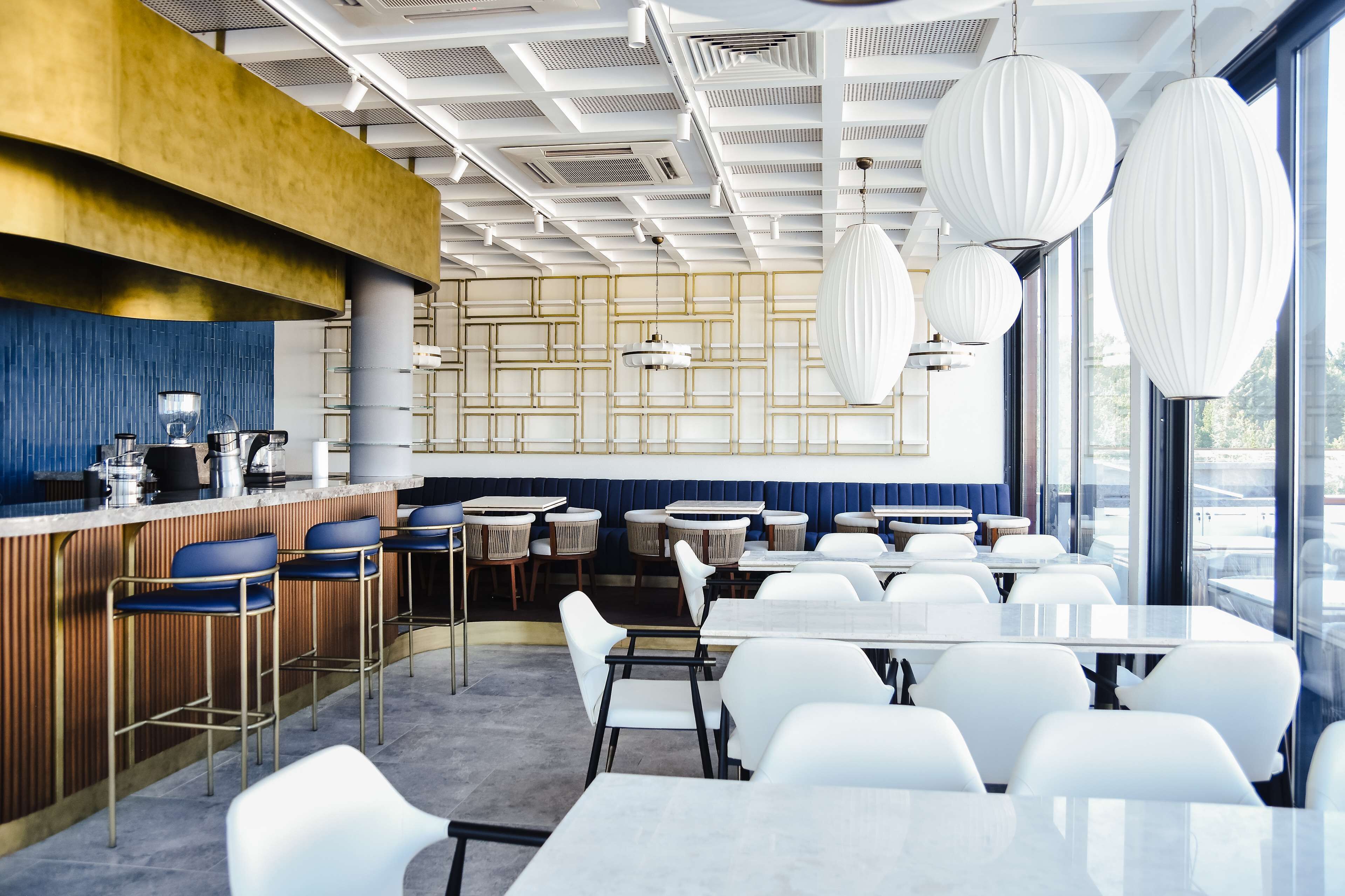 Ein modernes Restaurant mit Barbereich, weißen Tischen und hängenden Pendelleuchten.