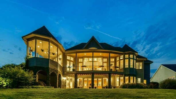 A large, multi-story house with a wrap-around porch, multiple windows, and a balcony. - Portside Villa Luxury Rental on Lake Gaston (Bracey)