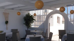 An outdoor dining area with wicker chairs and tables, a potted plant, and hanging spherical light fixtures. - Sagma Central (Santorini)