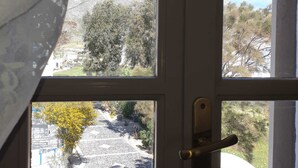 A door with a view of a mountainous landscape, a paved pathway, and some greenery. - Sagma Central (Santorini)