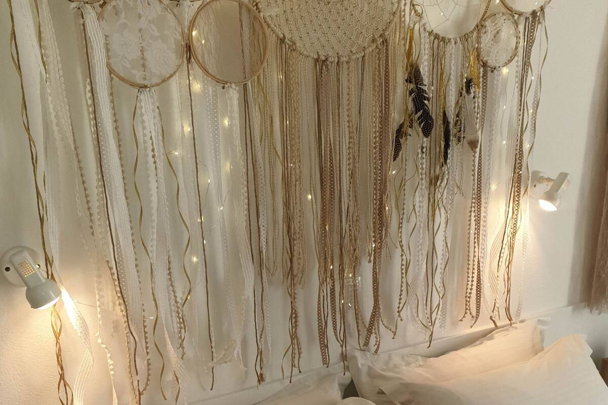A bedroom with a bed, pillows, and a hanging dreamcatcher with lights.