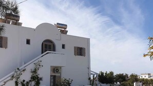 A white building with a stone-paved courtyard, a staircase, and a small garden area. - Sagma Central (Santorini)