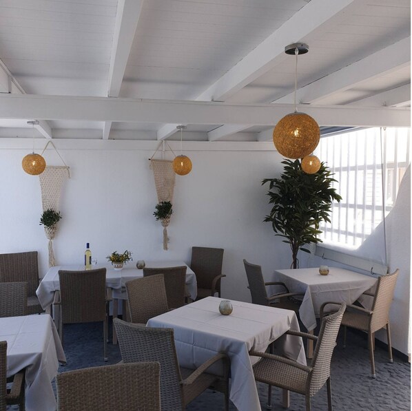 A restaurant with wicker furniture, white tablecloths, and hanging spherical light fixtures.