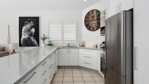 Enjoy cooking in this kitchen with a refrigerator, wall clock, and white cabinetry.