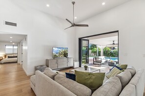 A spacious living room with a large sofa, a television, and a view of an outdoor patio with a pool.