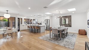 A modern kitchen with a central island, wooden flooring, and a dining area with a rug. - Casa De Sol - McCormick Ranch * 5BR w/ Heated Pool (Scottsdale)