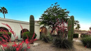 A landscaped garden with cacti, red flowering plants, and a building with arched windows. - Casa De Sol - McCormick Ranch * 5BR w/ Heated Pool (Scottsdale)