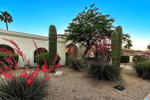 Un jardin aménagé avec des cactus, des plantes à fleurs rouges et un bâtiment doté de fenêtres en arc de cercle.