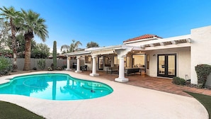 A pool with a curved edge, a covered patio area with outdoor furniture, and a building with a tiled roof. - Casa De Sol - McCormick Ranch * 5BR w/ Heated Pool (Scottsdale)
