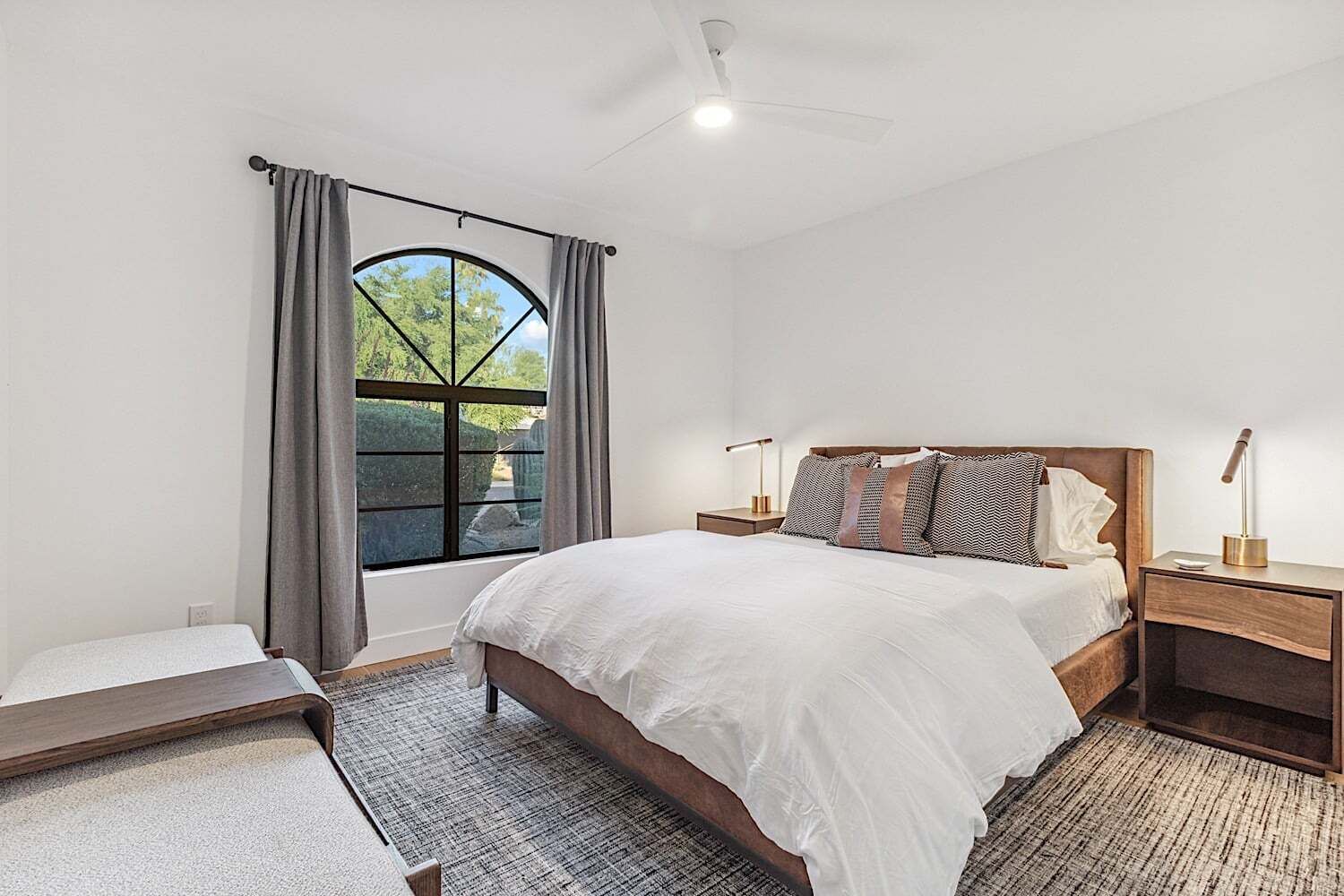 A bedroom with a large bed, two bedside tables, a window with curtains, and a ceiling fan.
