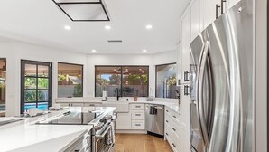 A modern kitchen with white cabinetry, stainless steel appliances, and large windows offering views of the outdoors. - Casa De Sol - McCormick Ranch * 5BR w/ Heated Pool (Scottsdale)
