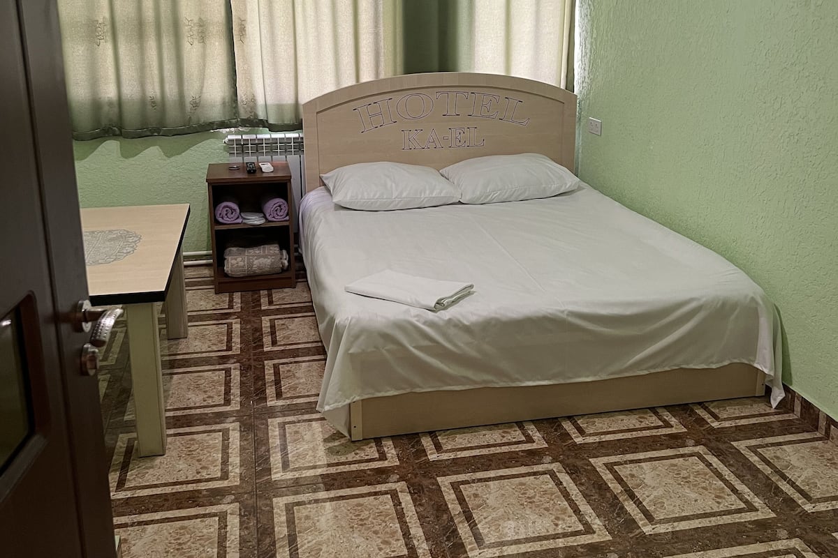 Una habitación de hotel con cama, mesita de noche, mesa y piso estampado.