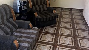 A living room with a sectional sofa, a striped armchair, a small table with a radio, and a potted plant. - Hotel KA-EL (Parakar)