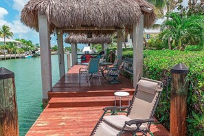 A wooden deck with chairs and tables, a thatched roof structure, and a view of the water. - My Beach Key~ Beach Membership, 32' Dock, Tiki Hut (Key Colony Beach)
