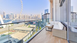 Ein Balkon mit Blick auf eine Stadtlandschaft, darunter ein Riesenrad, moderne Gebäude und ein Gewässer.