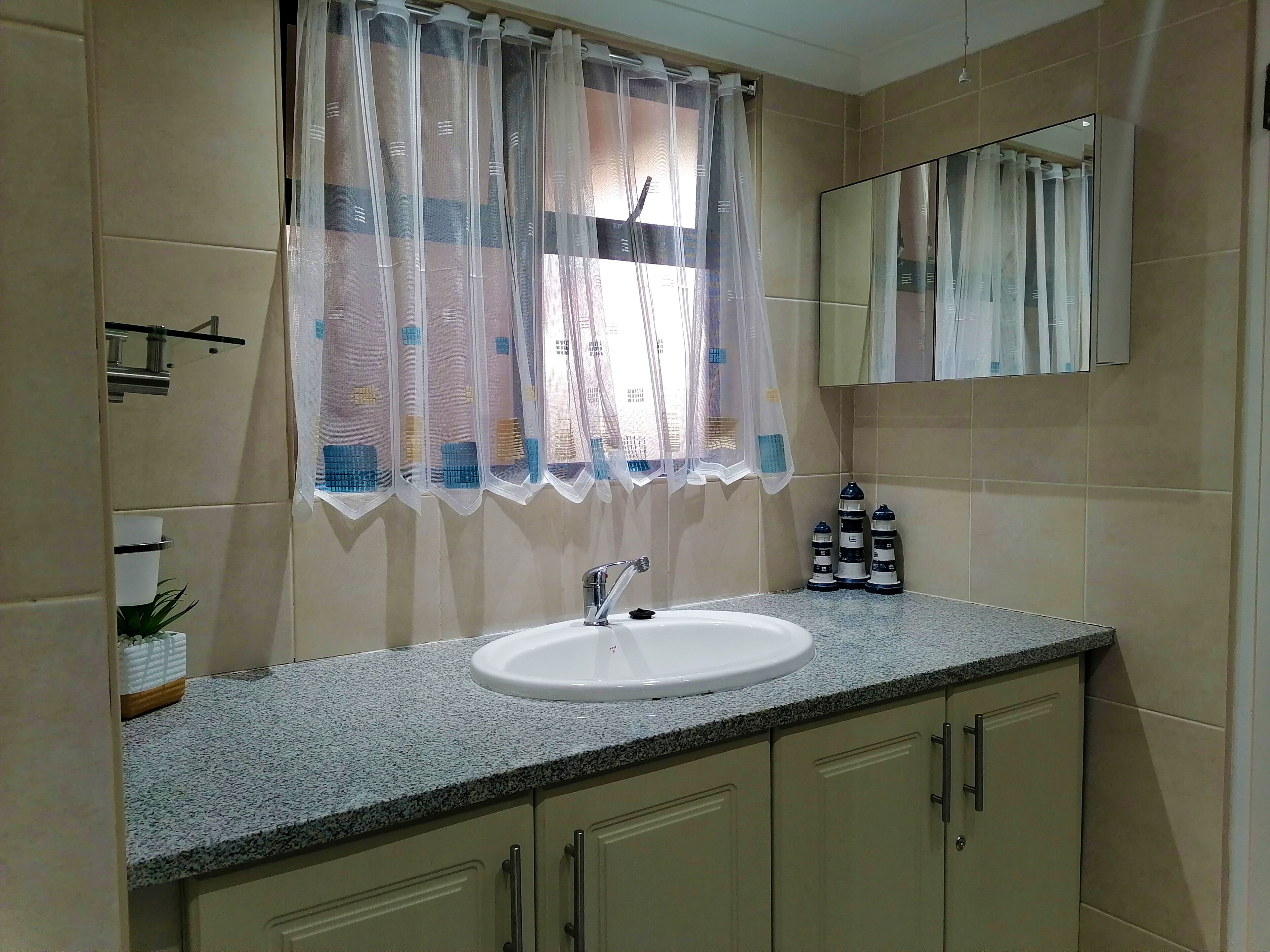 A bathroom with a sink, mirror, and window with sheer curtains.