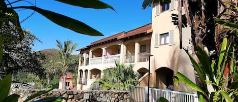 A two-story building with a balcony, a stone wall, and a lawn.