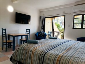 A bedroom with a bed, a desk, chairs, a TV, and a balcony with a view.