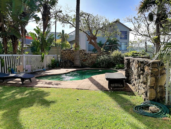 A backyard with a swimming pool, a stone wall, and a white fence.