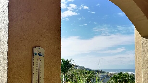 A balcony with a view of the beach, a thermometer, and a star decoration.